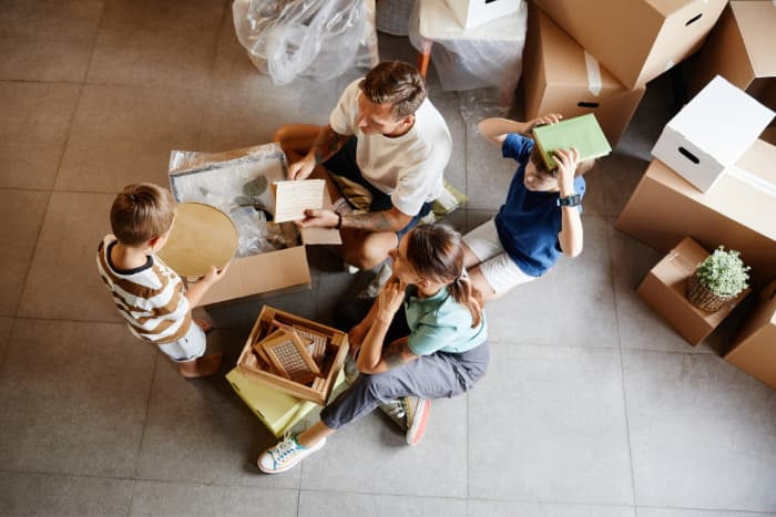 Top view portrait of family with two children moving into new house and unpacking boxes together, copy space