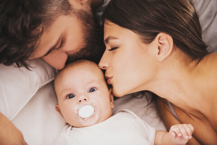 A young couple kissing their newborn at home
