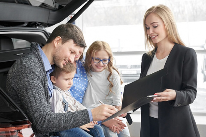 a family signs paperwork at the dealership to seal the deal on their new family car
